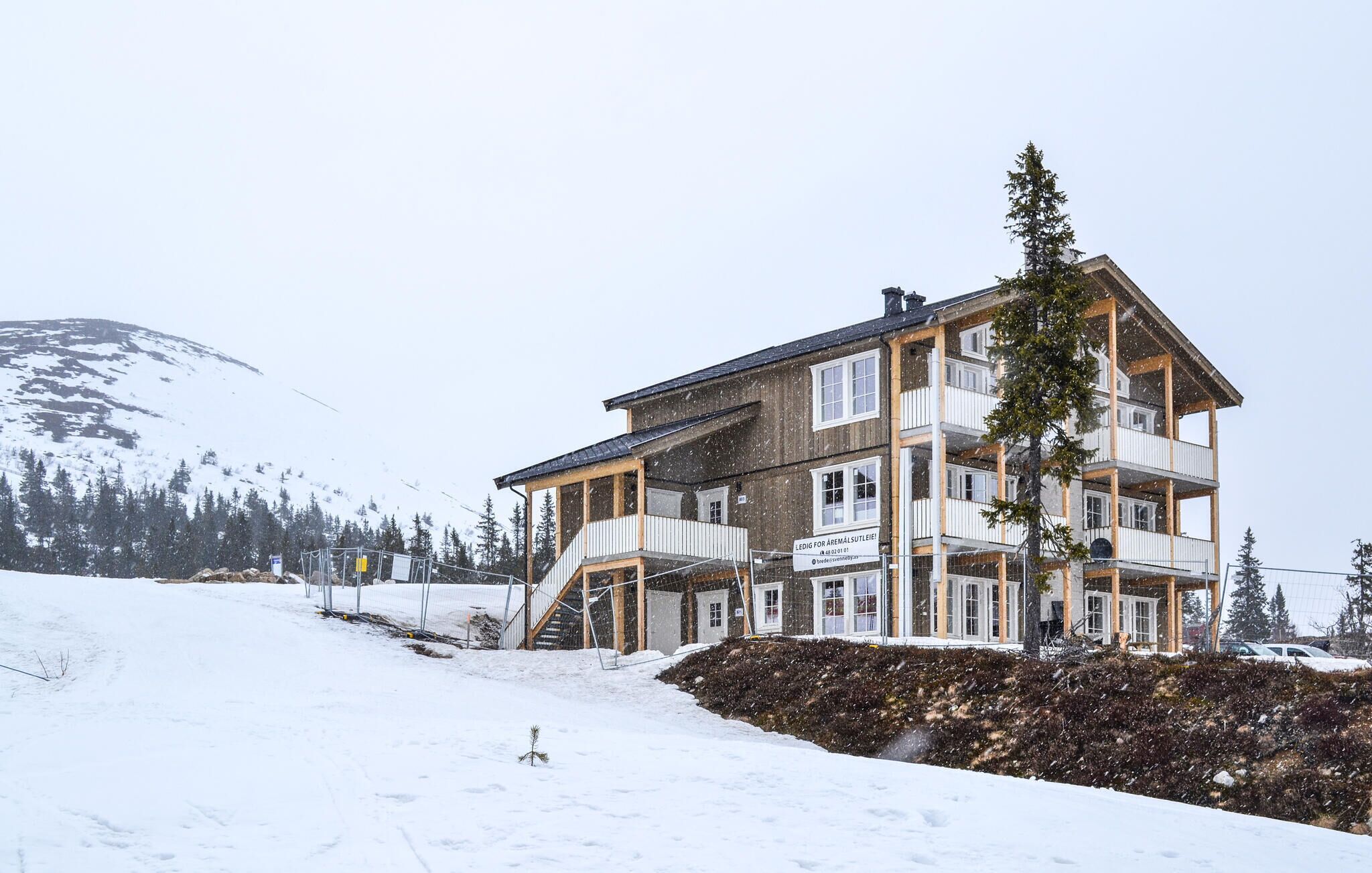 Un hotel a più piani con balconi, una pista da sci sullo sfondo e un paesaggio innevato.