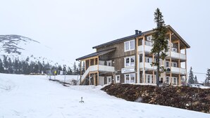 A multi-story hotel with balconies, a ski slope in the background, and a snowy landscape.