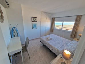 Een slaapkamer met een bed, bureau, stoel, raam met uitzicht en een deur.