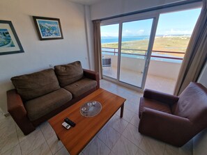 A living room with a brown sofa, a wooden coffee table, and a brown armchair. There is a large window with a view of a landscape. - TRAMUNTANA APARTMENT 12-04 (Roses)