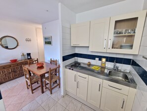 A compact kitchen with a dining area, featuring a wooden table, chairs, a sink, and cabinets. - TRAMUNTANA APARTMENT 12-04 (Roses)