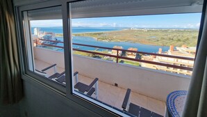 Un balcón con vista a un paisaje costero, que incluye una masa de agua y edificios a lo lejos.