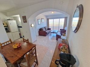 Een zithoek met een eettafel, stoelen, een bank en een salontafel. Er is een keuken met een koelkast, magnetron en fornuis. De kamer heeft een groot raam met uitzicht op het strand.