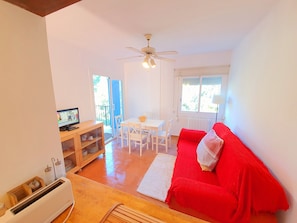 Ein Zimmer mit einem roten Sofa, einem weißen Esstisch, einem Deckenventilator und einem Fernseher.