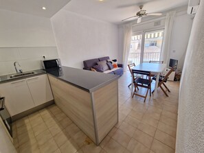 Een kleine keuken met een ingebouwde magnetron, een spoelbak en een eethoek met tafel en stoelen.