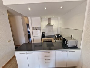 A compact kitchen with white cabinets, a black countertop, a built-in oven, a sink, and a stove. - APARTMENT BADIA 24 (Empuriabrava)