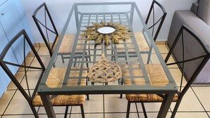 Une table à manger avec un plateau en verre, des chaises en osier, un élément décoratif au centre et un canapé gris en arrière-plan.