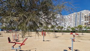 Un espace de remise en forme en plein air, équipé de matériel d’exercice, entouré d’arbres et avec un bâtiment en arrière-plan.