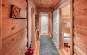 A wooden hallway with a fire extinguisher, a door, and a bed in the adjacent room. - Cozy home in Noresund with house a panoramic view (Noresund)