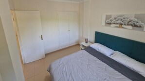 A bedroom with a bed, a nightstand, a wall-mounted shelf with a decorative item, and a door. - APARTMENT PALS BEACH-6 (Pals)
