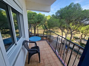 Een balkon met een tafel en stoelen, een uitzicht op bomen, en een hekwerk.