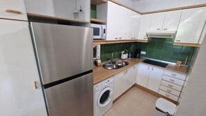 A compact kitchen with a stainless steel refrigerator, a washing machine, a microwave, and a sink. - APARTMENT PALS BEACH-6 (Pals)