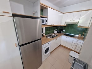 Een compacte keuken met een roestvrijstalen koelkast, een wasmachine, een magnetron en een spoelbak.