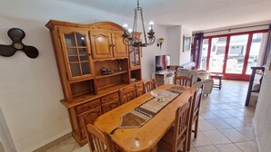 A dining area with a wooden table and chairs, a wooden cabinet with glass doors, a chandelier, and a television.