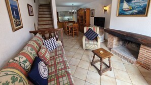 A living room with a sofa, a small table, a fireplace, a television, and a kitchen in the background.