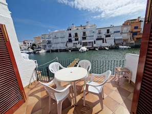 A terrace with a table and chairs, overlooking a marina with boats and buildings. - VILLA EMPORION CANALS (Empuriabrava)