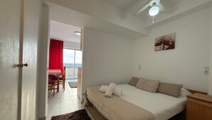 Une chambre à coucher avec un lit, un ventilateur de plafond, un tableau et une vue sur un balcon équipé d’une table et de chaises.