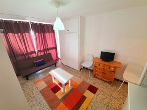 Ein Wohnzimmer mit einer Couch, einem weißen Couchtisch, einem Fernseher auf einem Holzschrank, einem weißen Sessel und einem gemusterten Teppich.