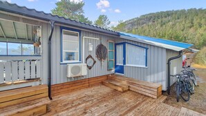 Une petite cabane à un seul étage, dotée d’un porche, d’une porte bleue et d’un vélo garé à l’extérieur.