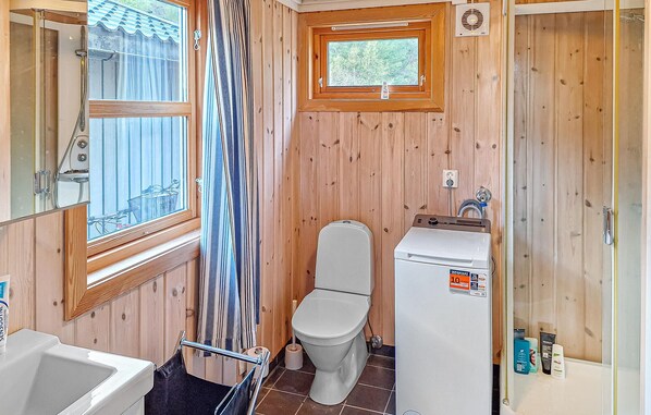 A compact bathroom with a shower, toilet, and sink, wooden walls, and a window.