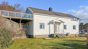 Een wit huis met twee verdiepingen, een balkon, een schoorsteen en een klein portaaltje.