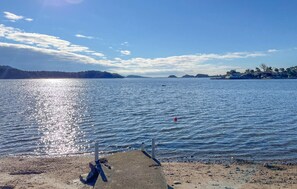A calm lake with a pier extending into the water, surrounded by hills and a clear sky.