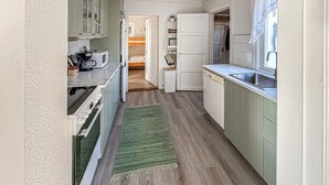 Een smalle keuken met een groen vloerkleed, houten vloeren en witte keukenkastjes.