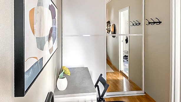 Un intérieur moderne comprenant un coin repas, un miroir et un couloir menant à une pièce dotée d’une porte et de patères.
