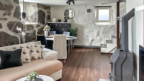Un salon avec un canapé, un coin repas avec des chaises, une cheminée et un mur en pierre.