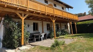 Un bâtiment à deux étages doté d’un balcon en bois et d’un espace extérieur aménagé avec des sièges, protégé par un auvent.