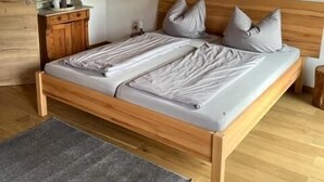 Un lit en bois dans une pièce dont le sol est également en bois, avec un tapis gris et une table de chevet en bois.