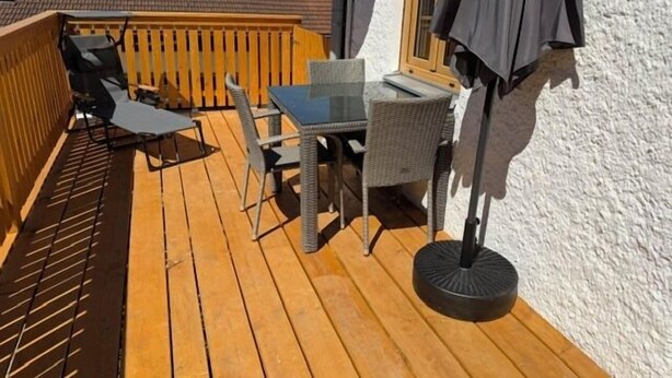 Une terrasse en bois, aménagée avec du mobilier d’extérieur, notamment une table et des chaises, et une fenêtre avec un rideau.