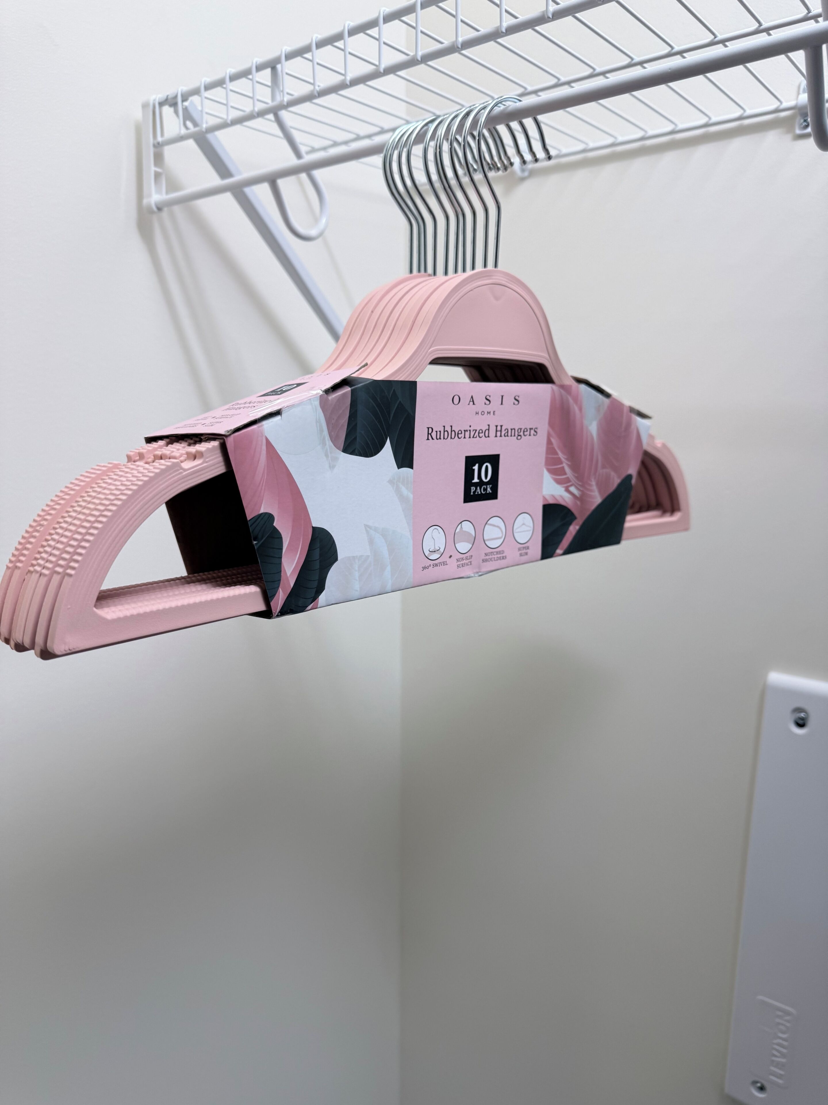 Ein pinkfarbener, gummiartiger Kleiderbügel mit floralem Muster, beschriftet mit 'Oasis Home Rubberized Hangers 10 Pack', an einem Metallgestell befestigt.