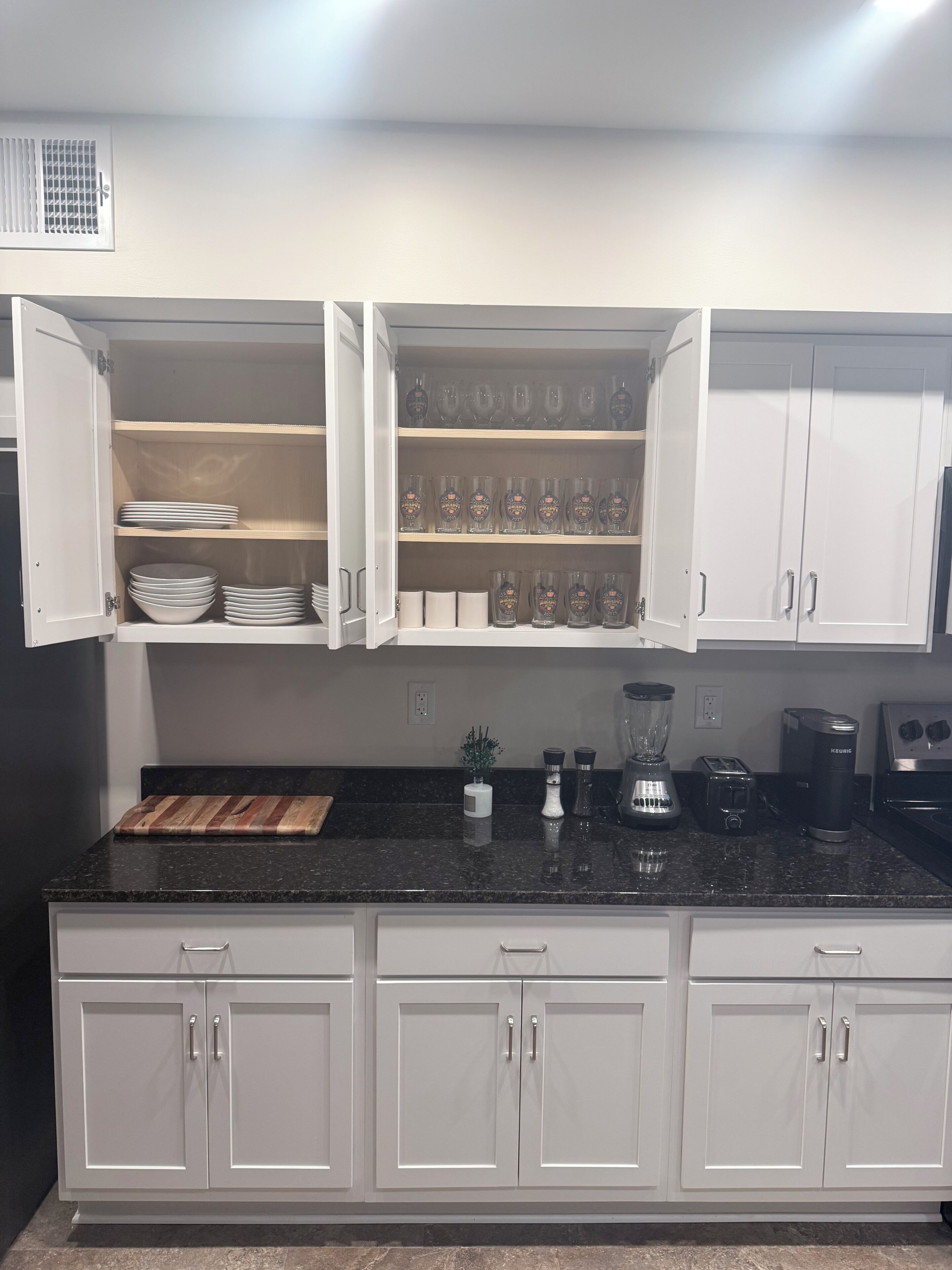 A kitchen with white cabinets, a black countertop, and various appliances including a blender, toaster, and kettle.
