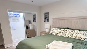 Une chambre à coucher comprenant un lit, une table de chevet, une lampe, un tableau et une porte donnant sur une salle de bain.