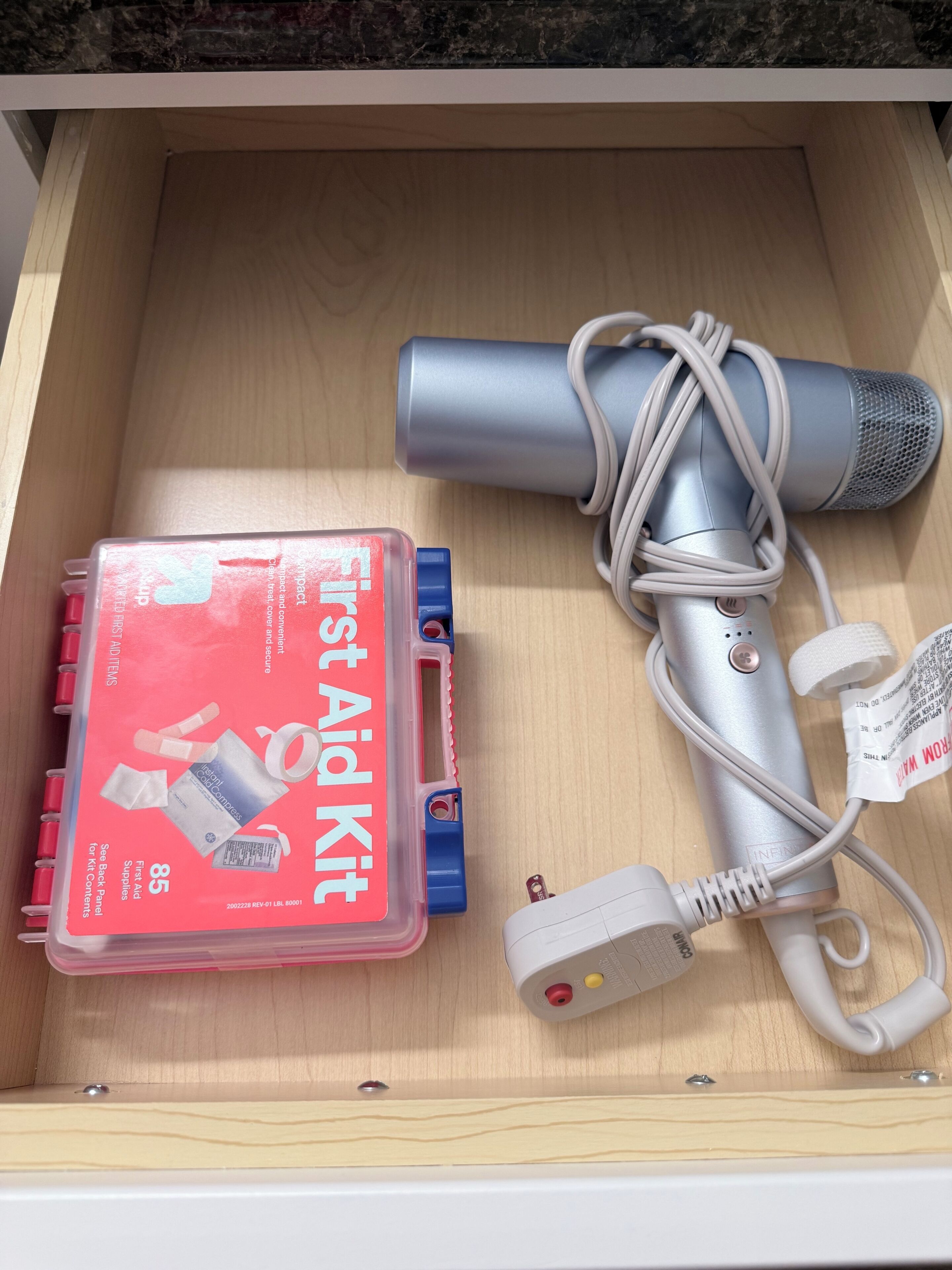 Un tiroir contenant une trousse de premiers secours, un sèche-cheveux et un adaptateur secteur.