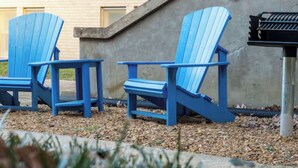 Trois chaises Adirondack bleues sont placées à l’extérieur d’un bâtiment doté d’un escalier en béton.
