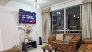 A living room with a leather sofa, a coffee table, a TV displaying a streaming service, and a large window with curtains. - Upscale 3BR Apt in Cusco,Gateway to Machu Picchu , Best Area (Cusco)