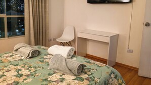 A hotel room with a bed, a desk, a chair, a TV, and a window with curtains. - Upscale 3BR Apt in Cusco,Gateway to Machu Picchu , Best Area (Cusco)