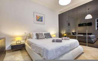 A modern bedroom with a large bed, bedside tables, a mirror, and artwork on the wall.