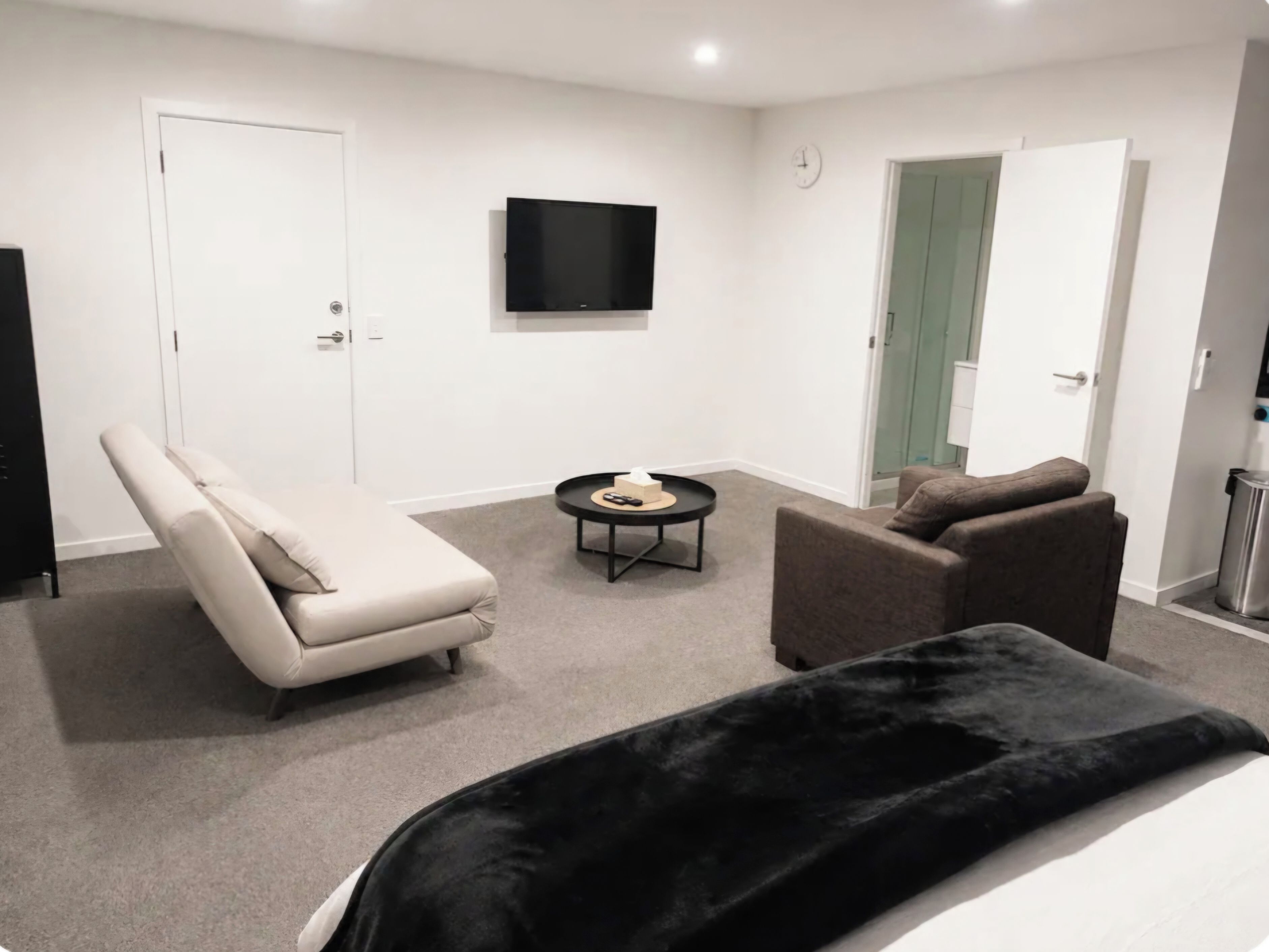 Ein modernes Hotelzimmer mit Bett, Sofa, Sessel, Fernseher und einem kleinen Tisch.