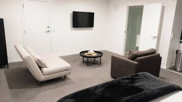 Ein modernes Hotelzimmer mit Bett, Sofa, Sessel, Fernseher und einem kleinen Tisch.