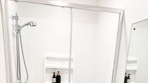 A modern bathroom with a glass-enclosed shower, a white sink with a mirror, and a shelf with toiletries. - Modern Gound Floor Studio (Cromwell)