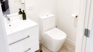 A bathroom with a white sink, mirror, toilet, and a door. - Modern Gound Floor Studio (Cromwell)