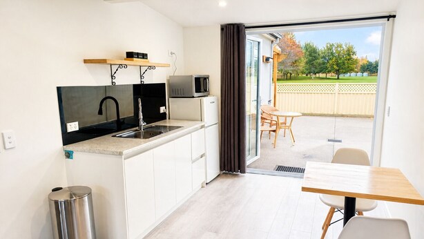 A modern kitchen with a sink, microwave, and cabinets, leading to a patio with a table and chairs. - Modern Gound Floor Studio (Cromwell)