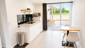 A compact kitchen with a sink, stove, and a small refrigerator. There is a dining area with a table and chairs, and a sliding glass door leading to an outdoor patio. - Modern Gound Floor Studio (Cromwell)