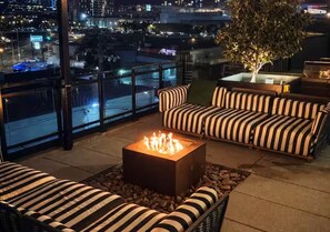 En tagterrasse med et bålsted, stribede sofaer og udsigt over bybilledet.
