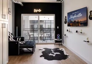 Un salon moderne avec un tapis en peau de vache noir et blanc, un canapé noir, une porte vitrée donnant sur l’extérieur et une pancarte indiquant « Bienvenue à Nashville ».