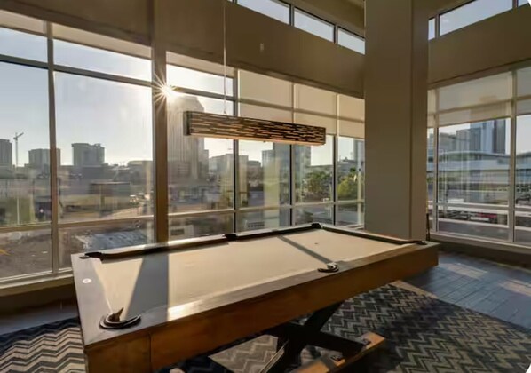 A pool table in a room with large windows offering a city view.