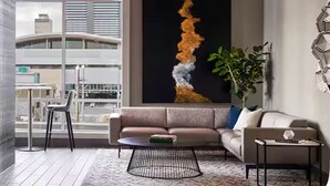 En moderne stue med sofa, sofabord og et stort abstrakt maleri på væggen.